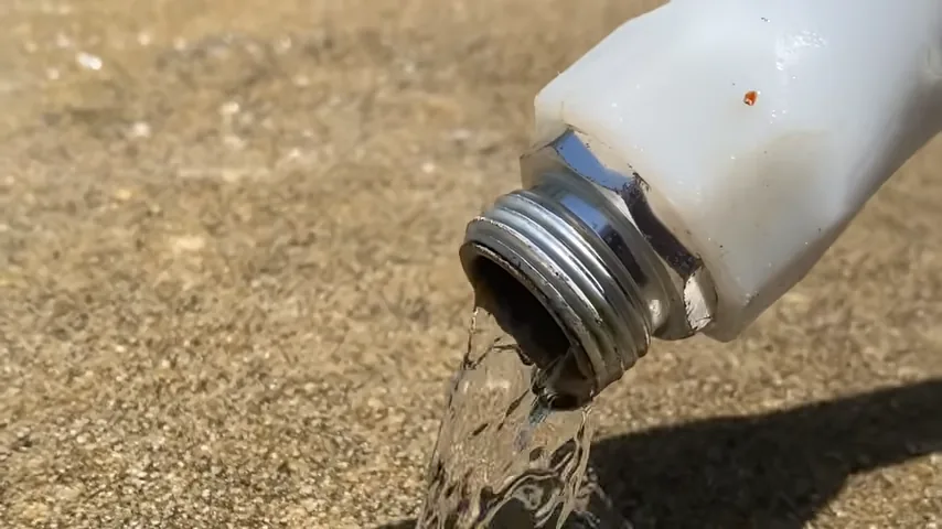 Water flowing from a white threaded pipe outlet into an outdoor drain area